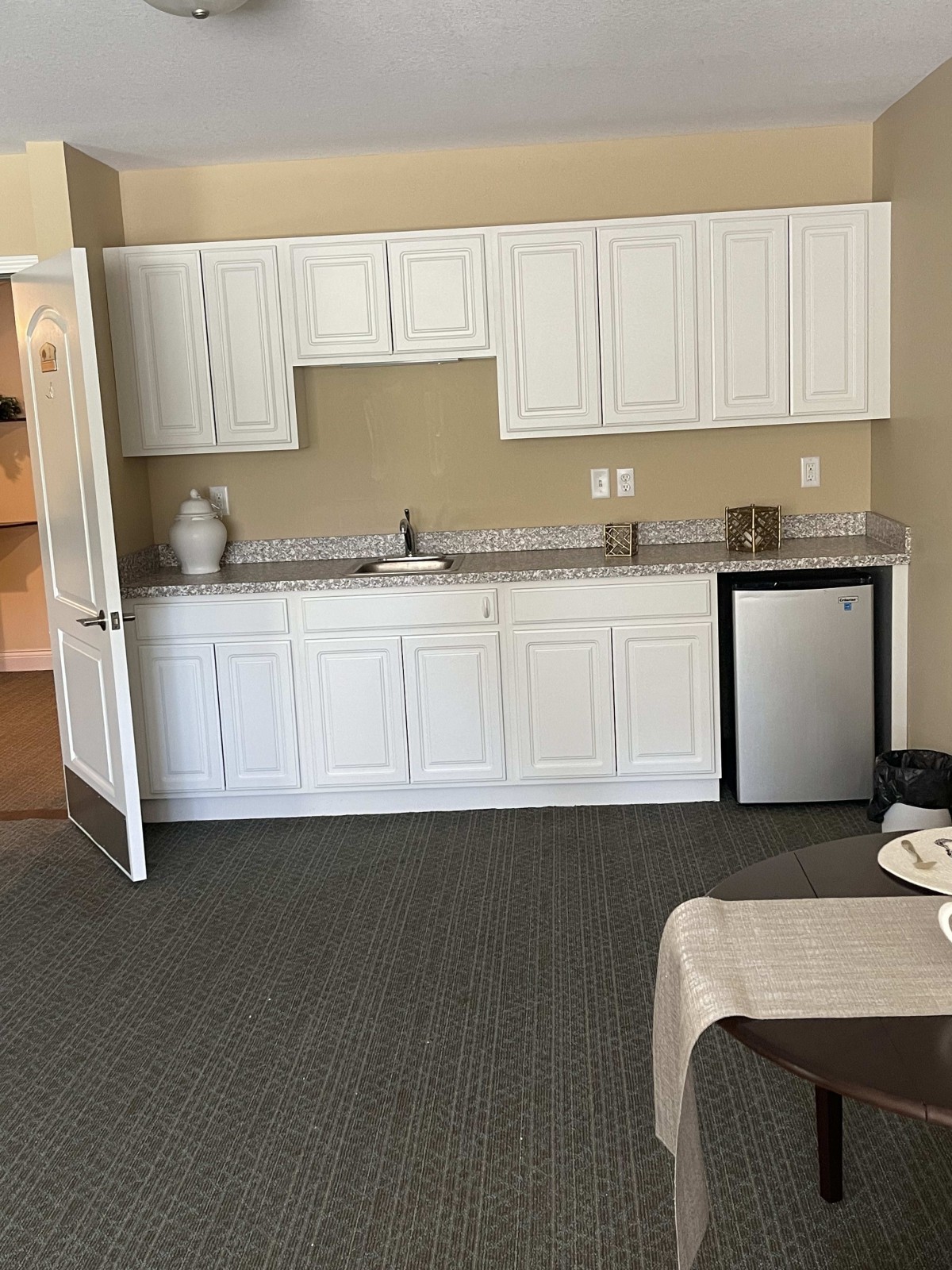 A kitchenette setup with white cabinets, a small sink, and a mini fridge.