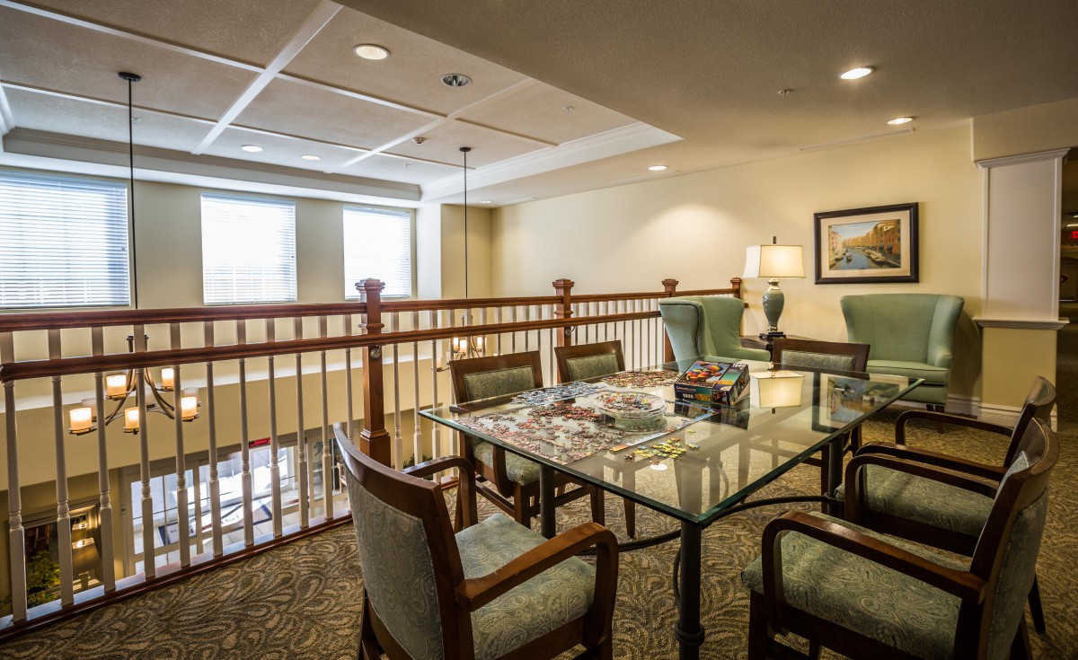 A cozy interior space featuring a table and chairs set, with a view of the railing and windows.