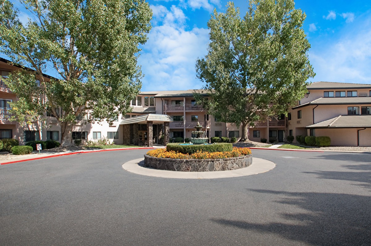 A well-landscaped building entrance with a roundabout, surrounded by trees under a partly cloudy sky.