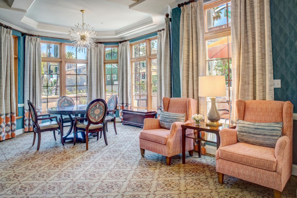 A spacious and elegantly decorated living room with traditional furniture, featuring large windows, a dining area, and a chandelier.