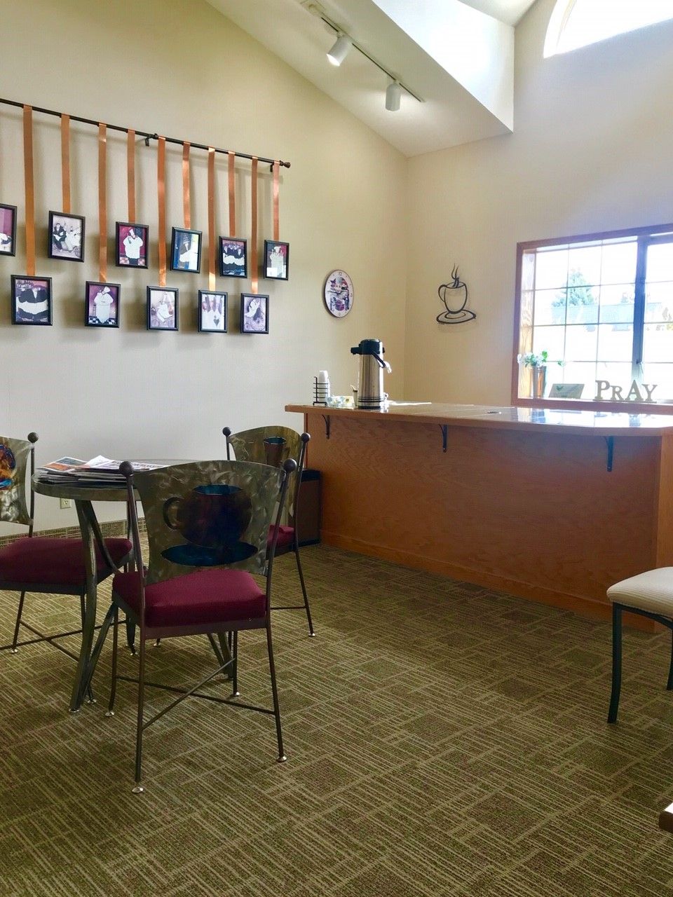 A cozy waiting room with chairs, a counter, and pictures on the wall, illuminated by natural light.
