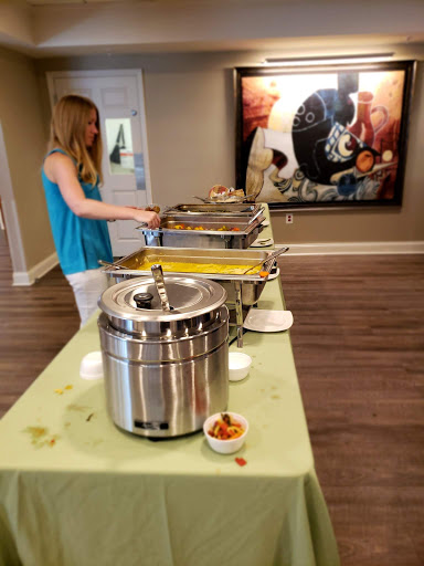 A woman serves food from a buffet setup during an event, showcasing a variety of dishes.