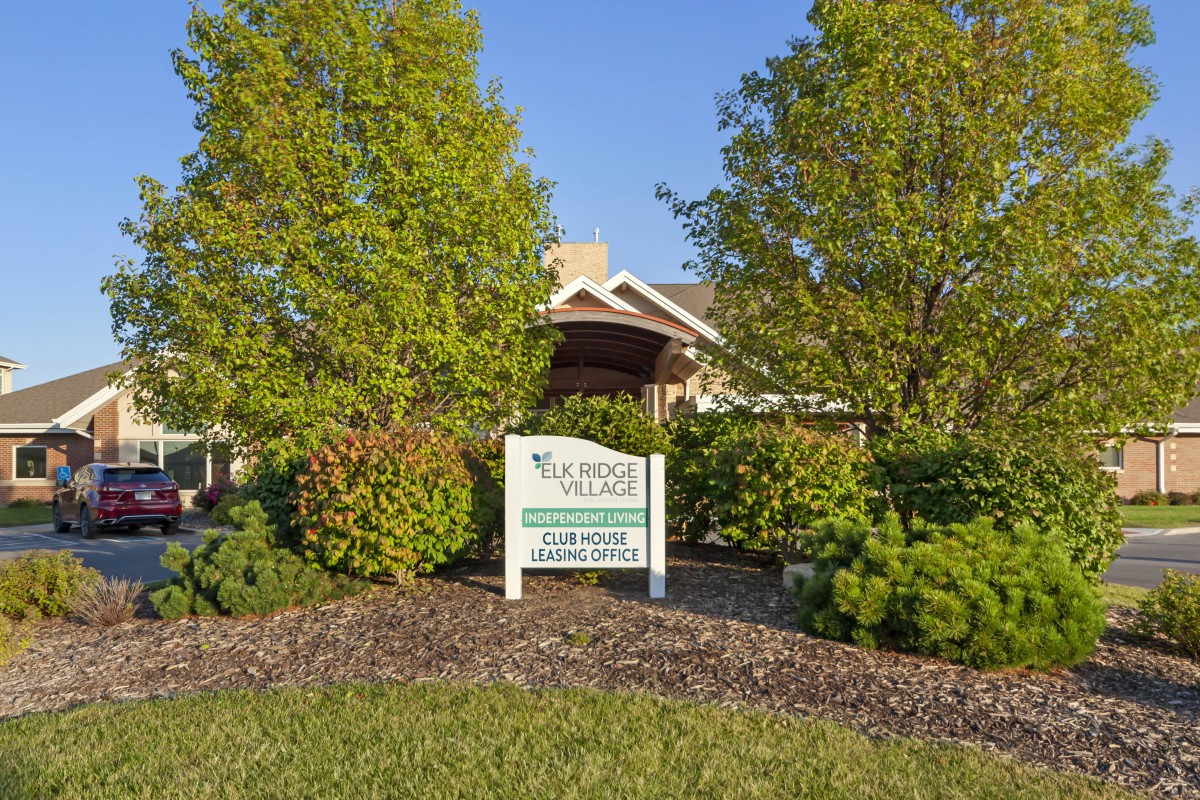 A building surrounded by lush greenery and a sign out front on a sunny day.