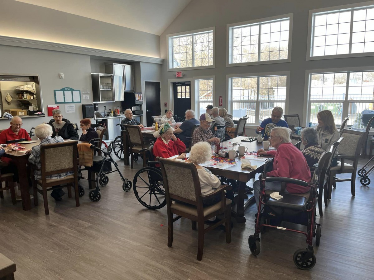 Elderly residents gathered in a nursing home common area, engaging in social activities.