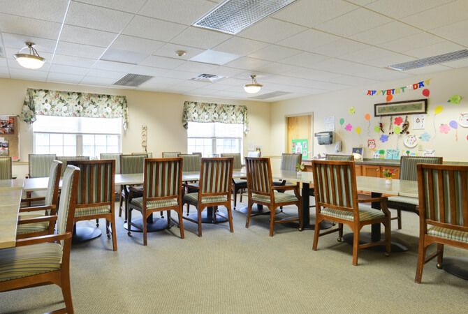 A spacious conference room with a long table and multiple chairs, well-lit by natural light from two windows.