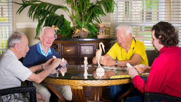 A group of seniors engaged in woodcarving around a table, enjoying their hobby indoors.