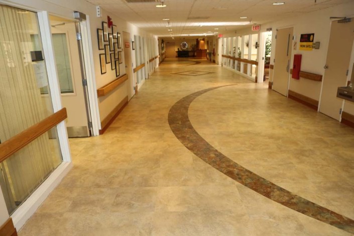 An empty hallway with tiled flooring and bright lighting in a hospital or care facility.