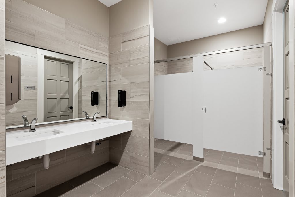 A modern public restroom with a large mirror, sink, and toilet stalls.