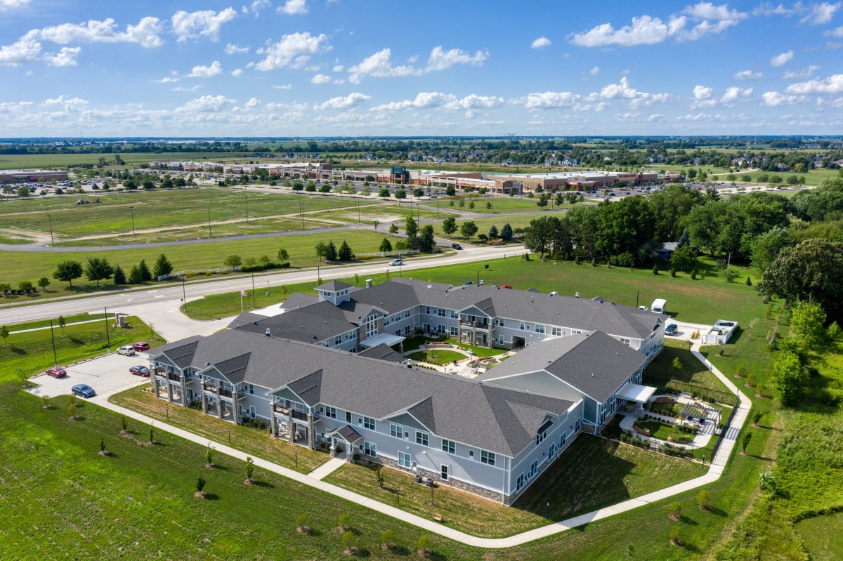 Aerial view of a large residential building surrounded by greenery and open fields under a partly cloudy sky.