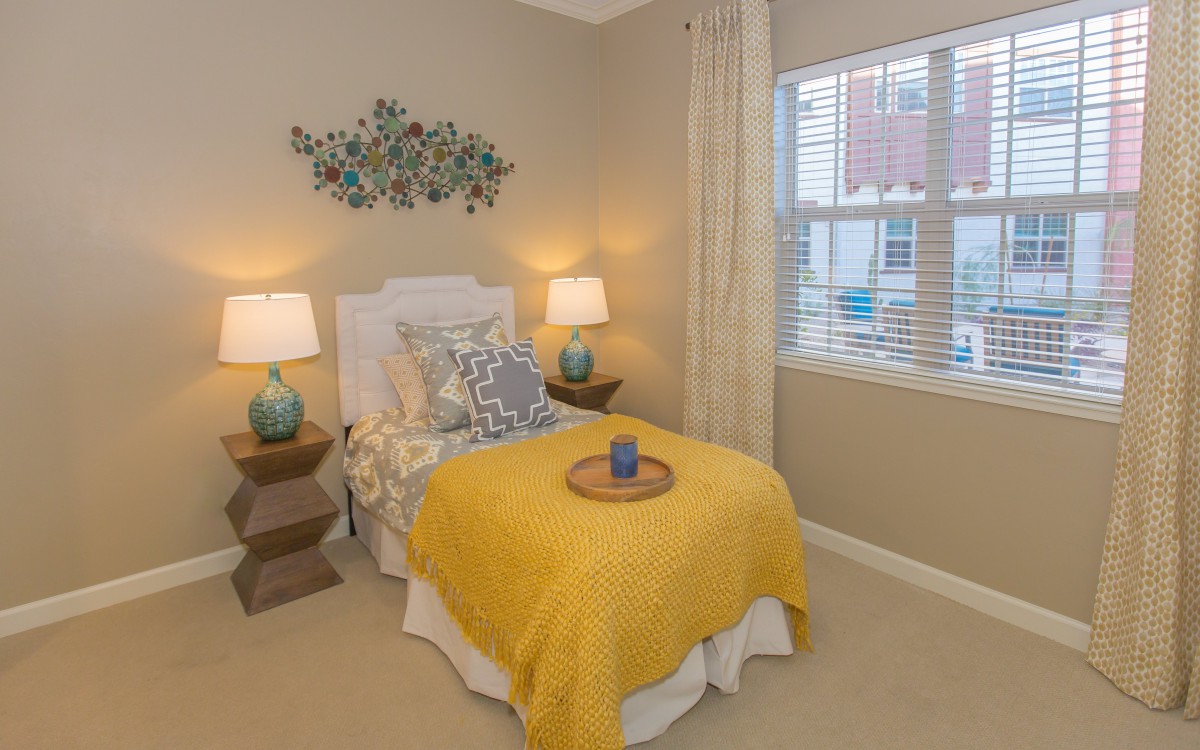 A cozy bedroom with a single bed, decorated with a yellow blanket and pillows, flanked by two bedside lamps.