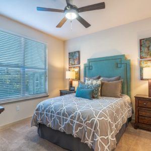 A modern bedroom with stylish decor, featuring a bed with a patterned duvet, bedside tables with lamps, and a ceiling fan.