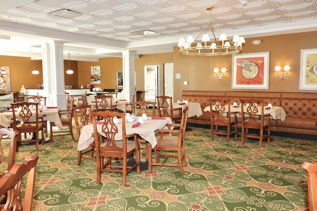 A well-furnished dining area with wooden tables and chairs, adorned by a chandelier and patterned carpet.