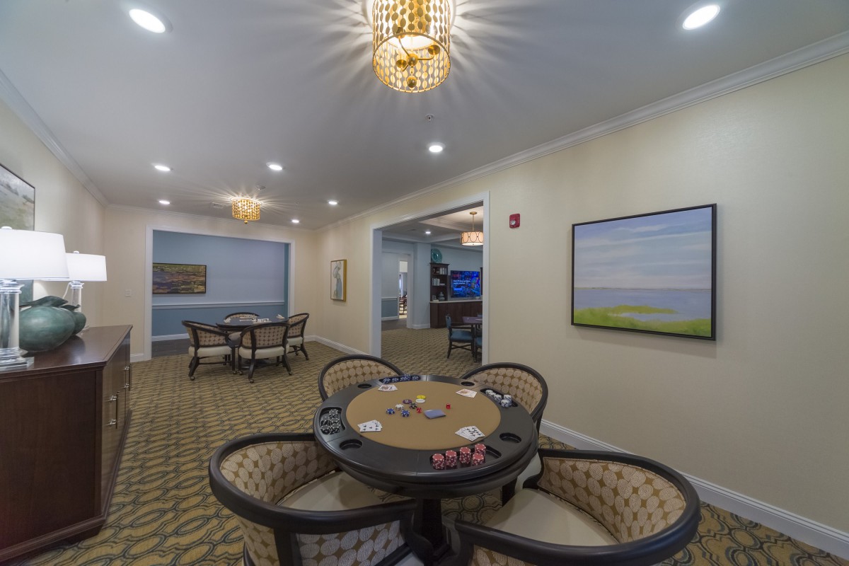 A well-furnished interior room featuring a round card table with chairs, elegant chandeliers, and wall artwork.