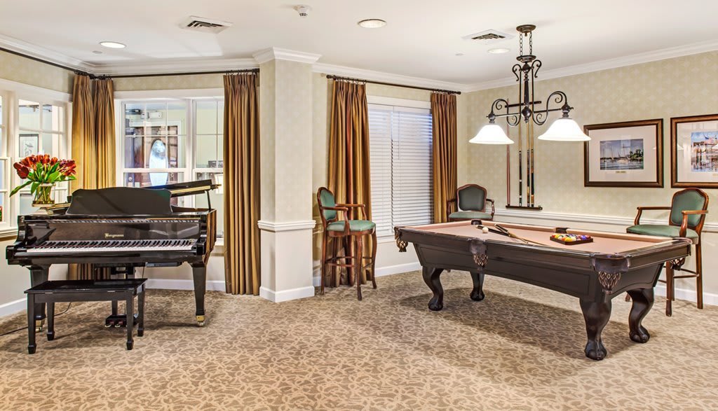 A cozy room featuring a grand piano and a pool table under a chandelier.