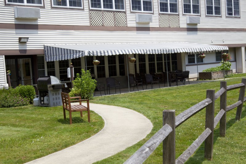 A building with an awning covering outdoor seating and a landscaped lawn in front.