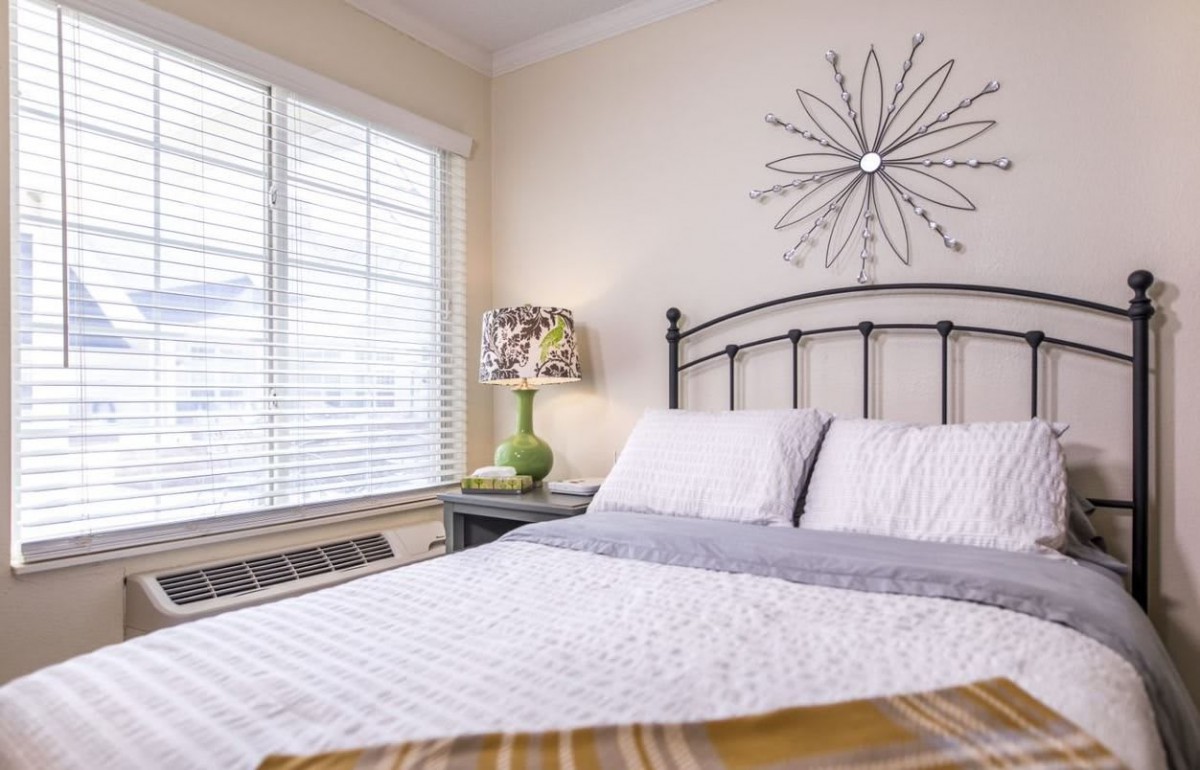 A cozy bedroom with a neatly made bed, decorative wall art, and a lamp by the window.