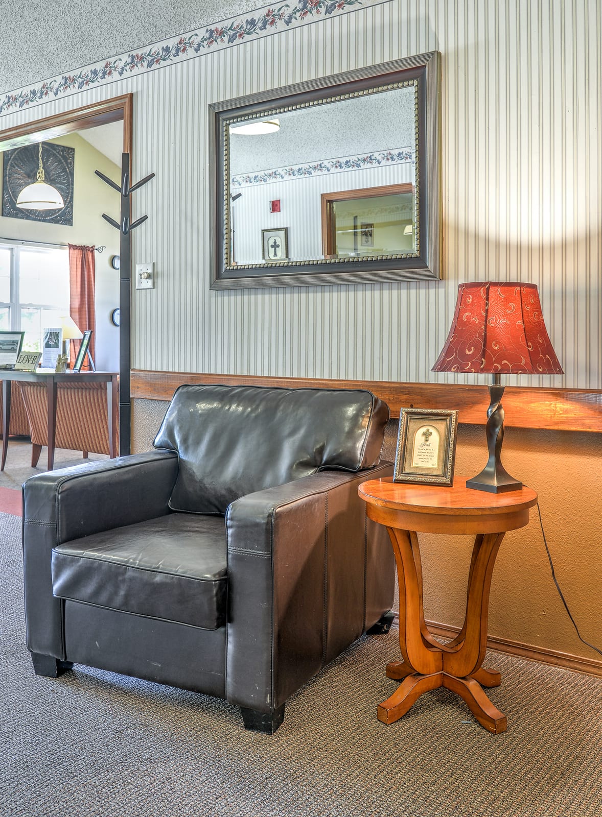 A cozy waiting area featuring a leather armchair and a wooden side table with a lamp.