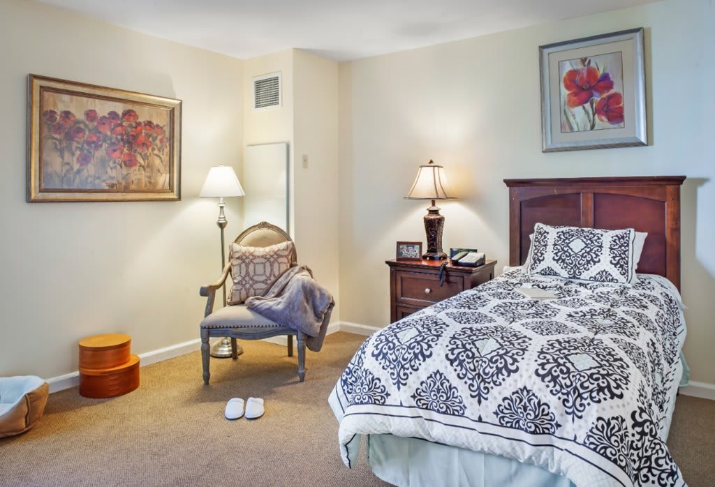 A cozy bedroom with patterned bedding, a chair, and decorative lamps.