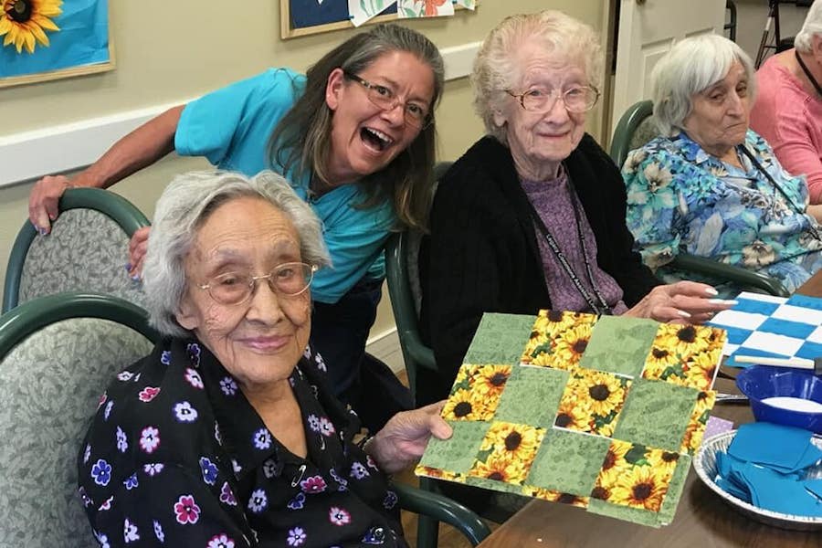 Three women smiling together, with one holding a sunflower-themed artwork.