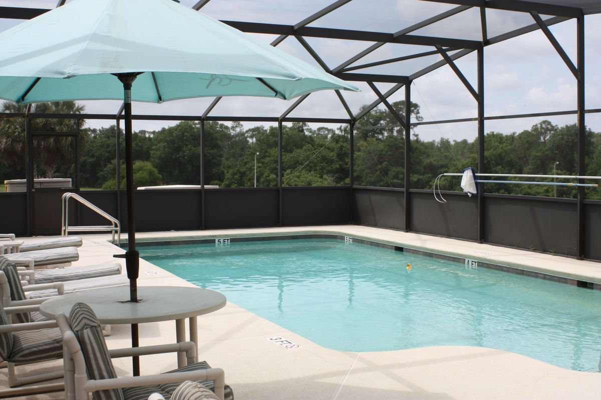 An outdoor pool with a screened enclosure and patio furniture, including an umbrella.