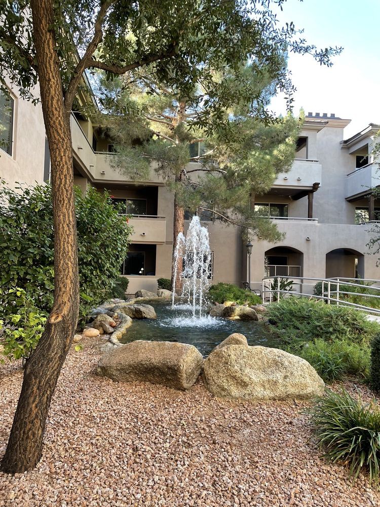A serene apartment courtyard with a central fountain surrounded by trees and rocks.