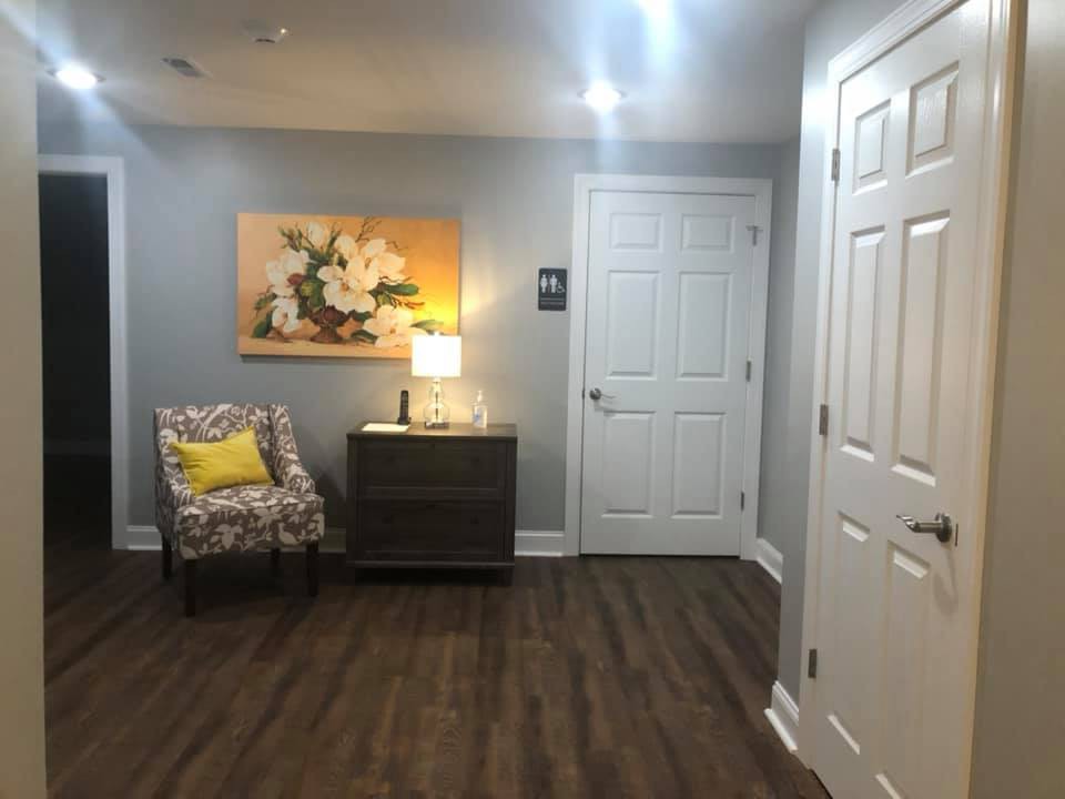 A cozy interior room with a floral chair, a lamp on a side table, and decorative artwork on the wall.