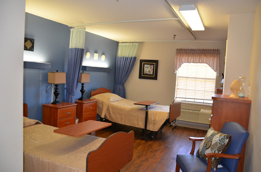 A well-lit hospital room featuring two beds, wooden furniture, and a cozy atmosphere.