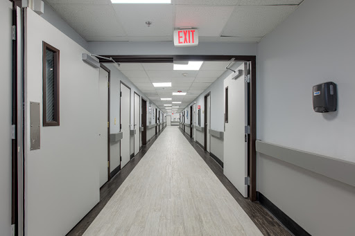 A wide view of a hospital hallway with multiple doors and bright lighting.