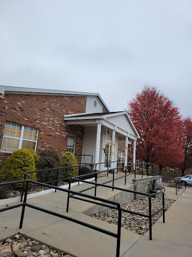 A brick building with an accessibility ramp, surrounded by autumn foliage under a cloudy sky.