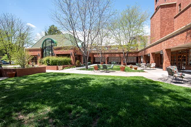 A view of a brick building with a green lawn and trees on a sunny day.