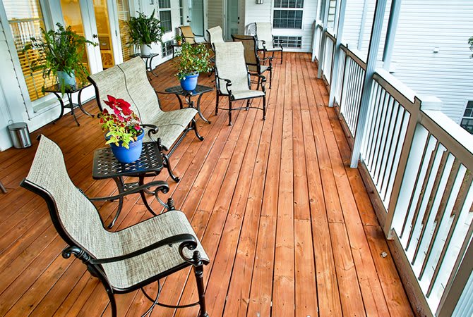 A cozy porch with wooden flooring, featuring chairs, tables, and potted plants.