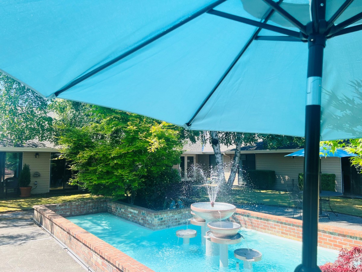 A tranquil outdoor scene with a blue umbrella shading a small fountain and pool.