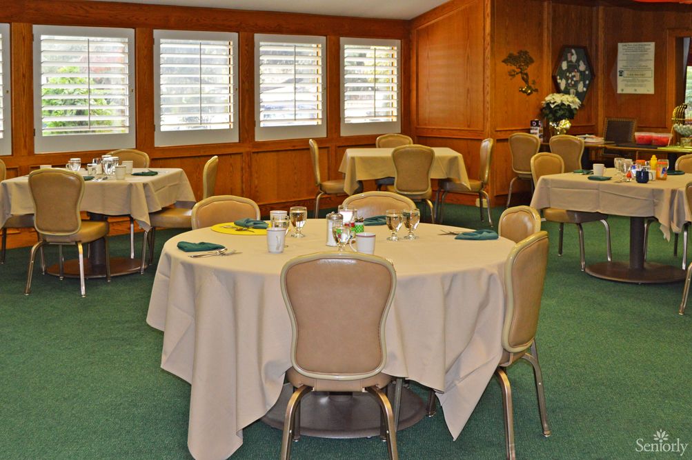 A well-arranged dining room with round tables and chairs, featuring white tablecloths and large windows.