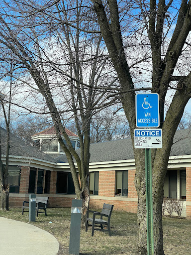 A blue handicap parking sign stands in front of a public building, surrounded by bare trees.