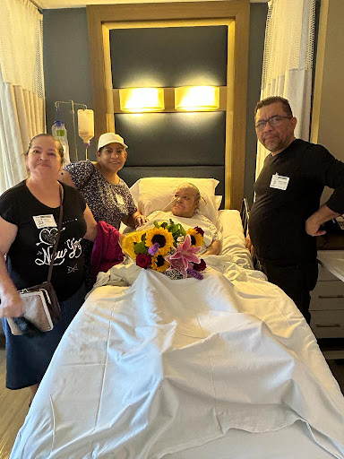 A heartfelt moment with family gathered around a loved one in a hospital setting, surrounded by flowers.