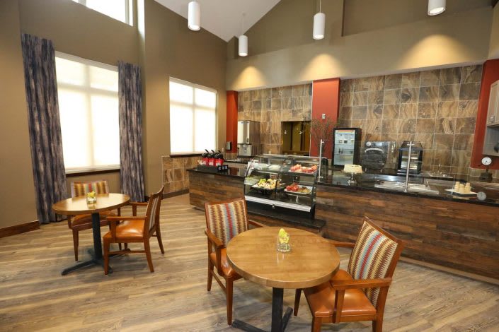 A cozy cafe interior with a seating area featuring wooden tables and chairs, illuminated by overhead lights.