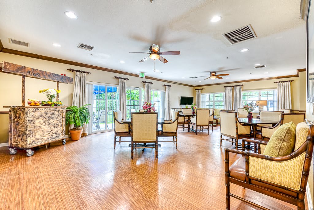 A spacious and well-lit dining area with multiple tables and chairs, ceiling fans, plants, and large windows allowing in natural light.