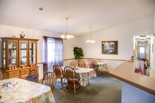 A cozy dining room setup with wooden tables and chairs, decorated with soft lighting and a touch of greenery.