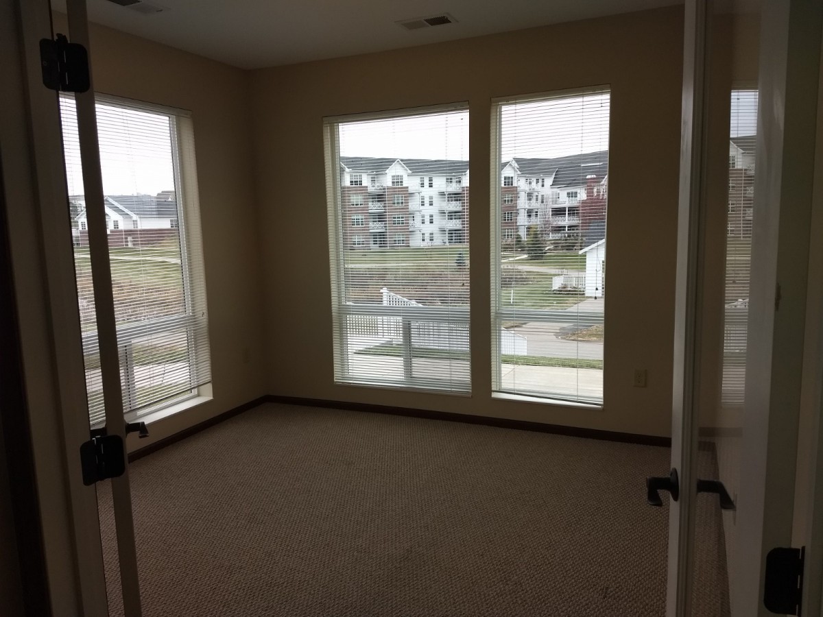 An empty bedroom in an apartment with large windows letting in natural light.