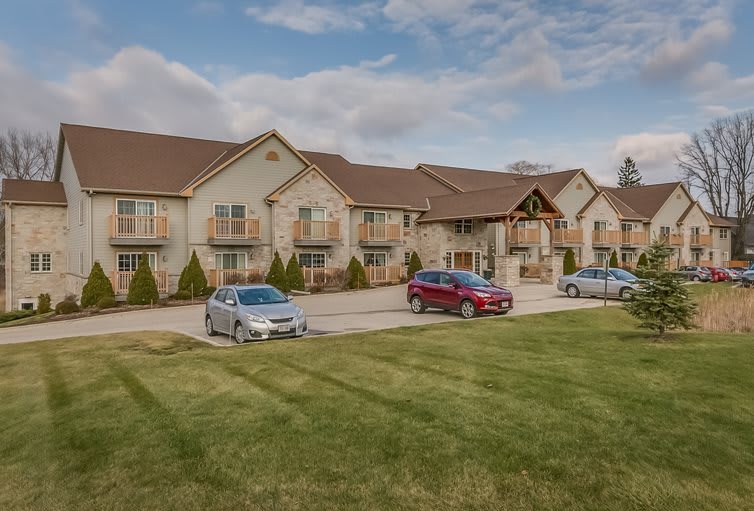 A residential apartment complex with cars parked in front, surrounded by a well-maintained lawn under a cloudy sky.
