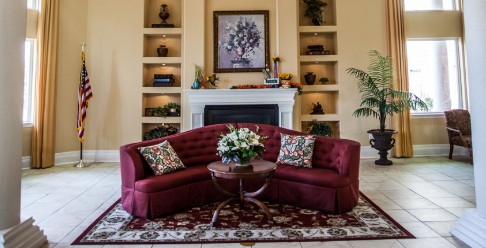 A cozy living room with a red sofa, floral centerpiece, and elegant fireplace surrounded by built-in shelves.