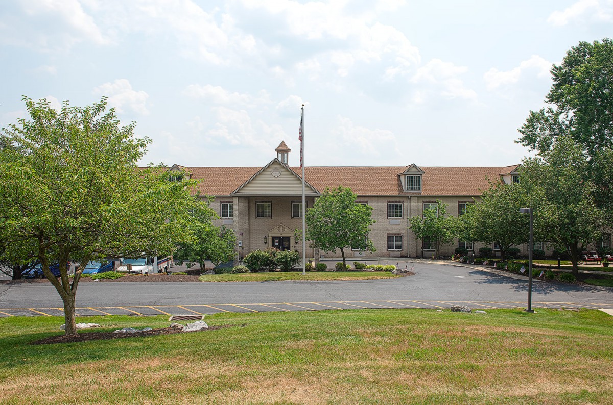 A hotel building with a parking lot and surrounding trees.