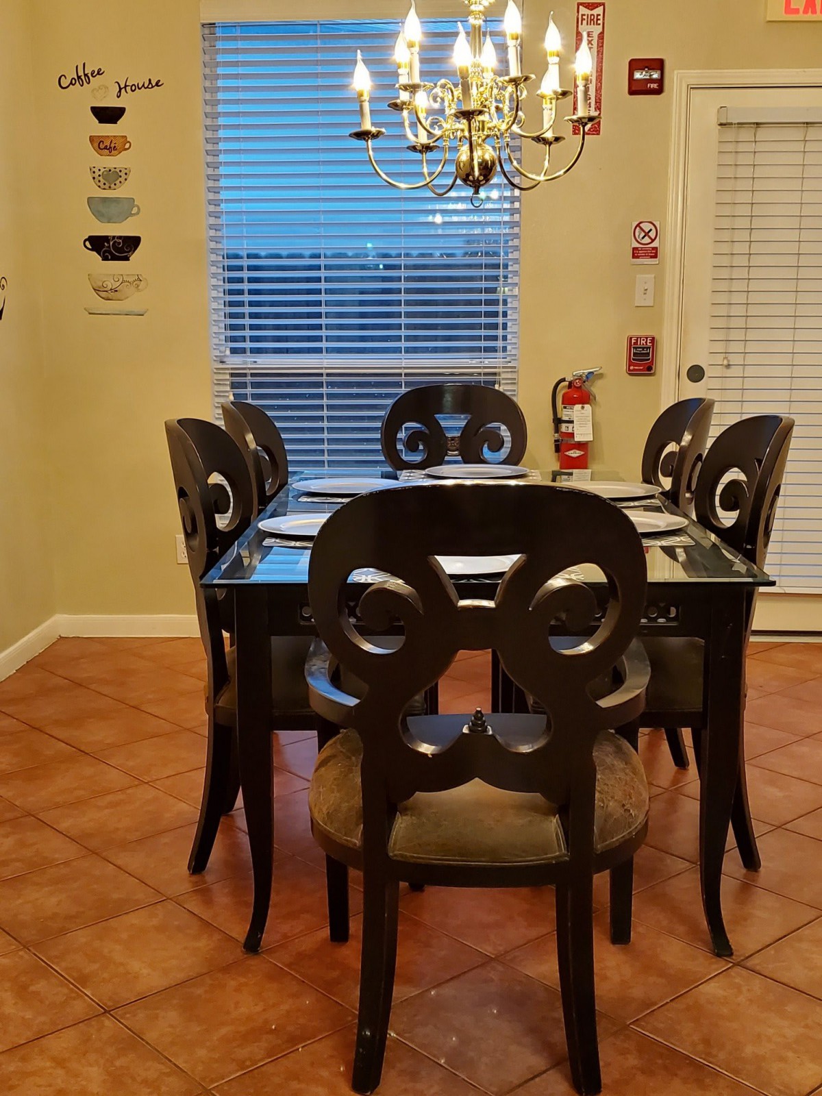 A cozy dining room with a glass-top table and six ornate chairs under a chandelier.