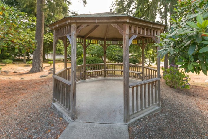 A wooden gazebo in a park setting surrounded by trees.
