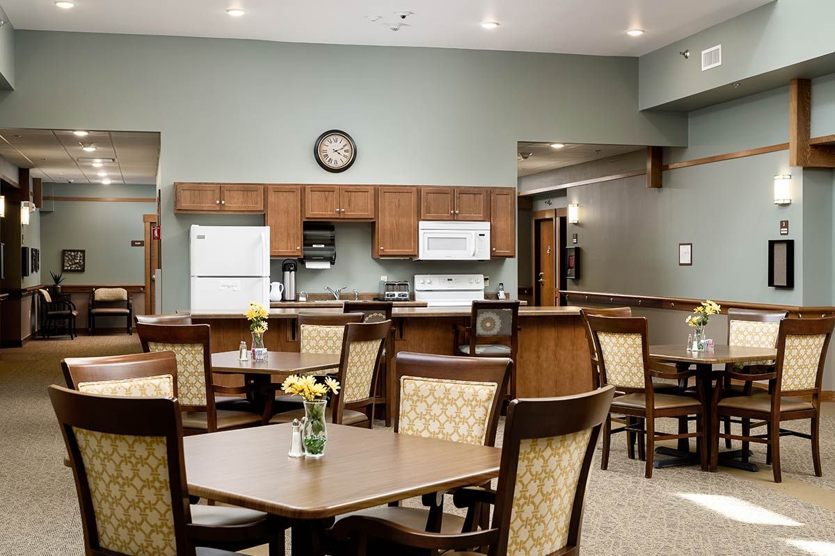 A cozy kitchen and dining area featuring several tables and chairs with wooden cabinetry and appliances.