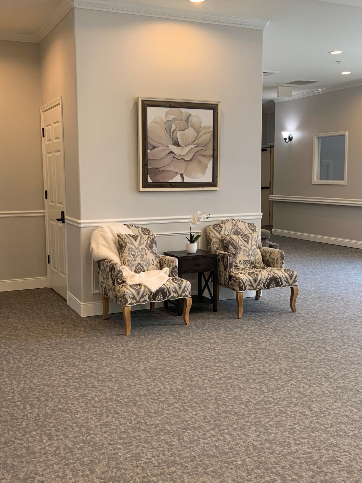 A cozy waiting area with two floral-patterned chairs and a small table, complemented by a painting on the wall.