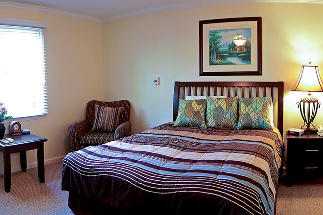 A well-decorated bedroom featuring a comfortable bed with patterned bedding, an upholstered chair, and a framed painting on the wall.