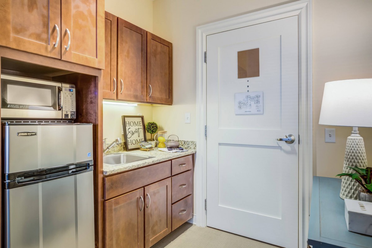 A small kitchen area with wooden cabinets, a sink, and a refrigerator next to a door.