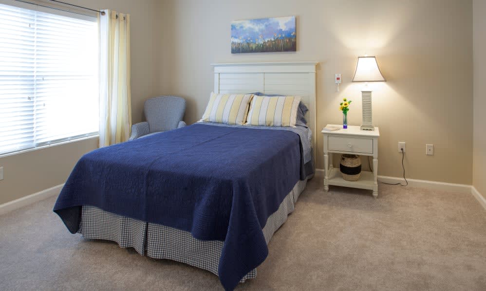 A cozy bedroom with a neatly made bed featuring blue bedding, accompanied by a nightstand and lamp.