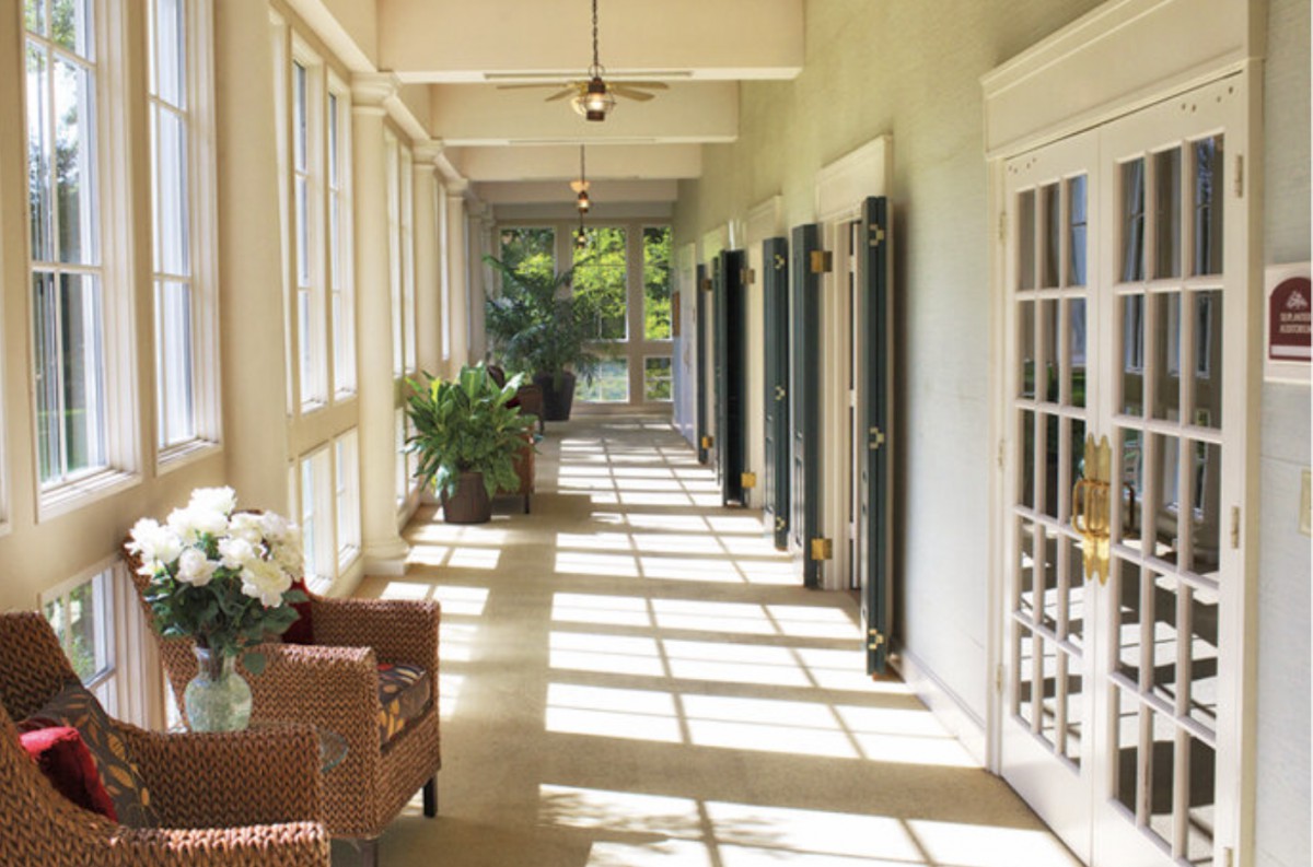 A bright sunroom hallway with large windows, letting in natural light and featuring comfortable furniture and indoor plants.